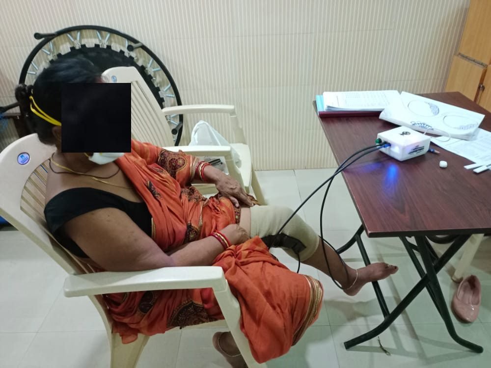 A person resting in a chair during a SwaKnee session, with the device on a side table (identity obscured)